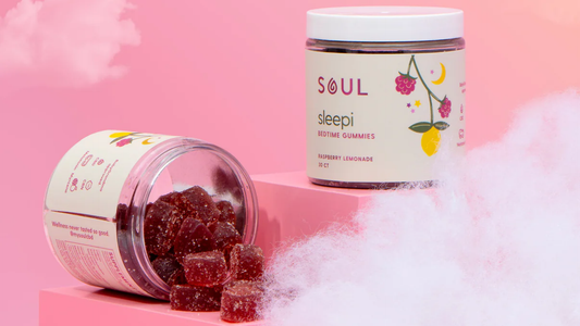 Front-right view of Sleepi bedtime gummies jar showing spilled raspberry lemonade gummies and label on a pink cloud background