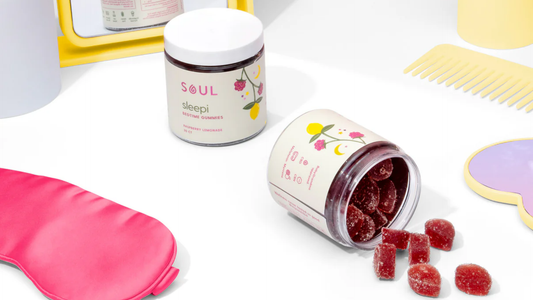 Front view of SOUL Sleepi bedtime gummies jar and open jar spilling sugar-coated raspberry lemonade gummies on white surface