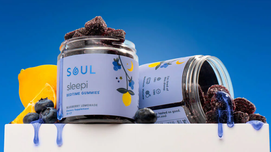 Close up of Soul Sleepi bedtime gummies jars with blueberry lemon gummies spilling onto white surface against blue background