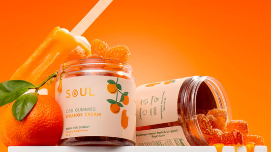 Close-up of Soul CBD Gummies Orange Cream jar with orange gummies spilling out and an orange popsicle against an orange background