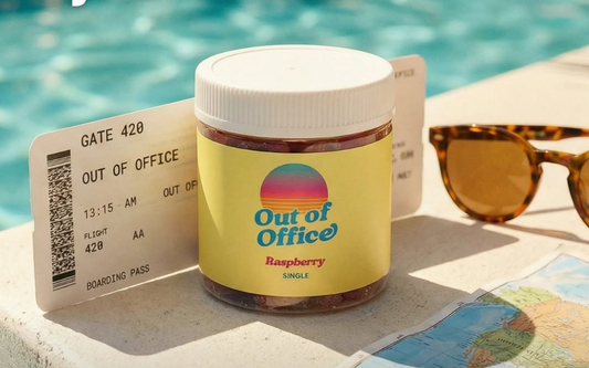 Front view of Out of Office raspberry gummies jar with yellow label beside a boarding pass, sunglasses, and a map by a pool