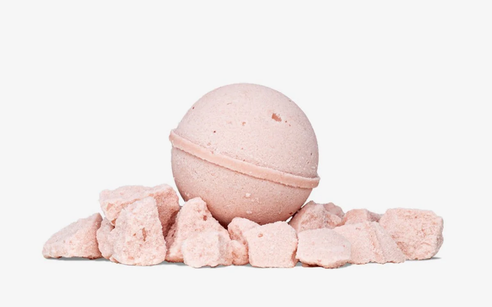 Front view of pink bath bomb resting on crushed pink bath salts with white background