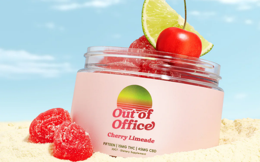 Close-up of Out of Office Cherry Limeade jar with red sugar-coated gummies, lime wedge and cherry on sand and blue sky background