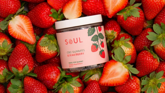 Angled jar of Soul strawberry CBD gummies showing pink label SOUL CBD Gummies Strawberry 10 mg among fresh strawberries