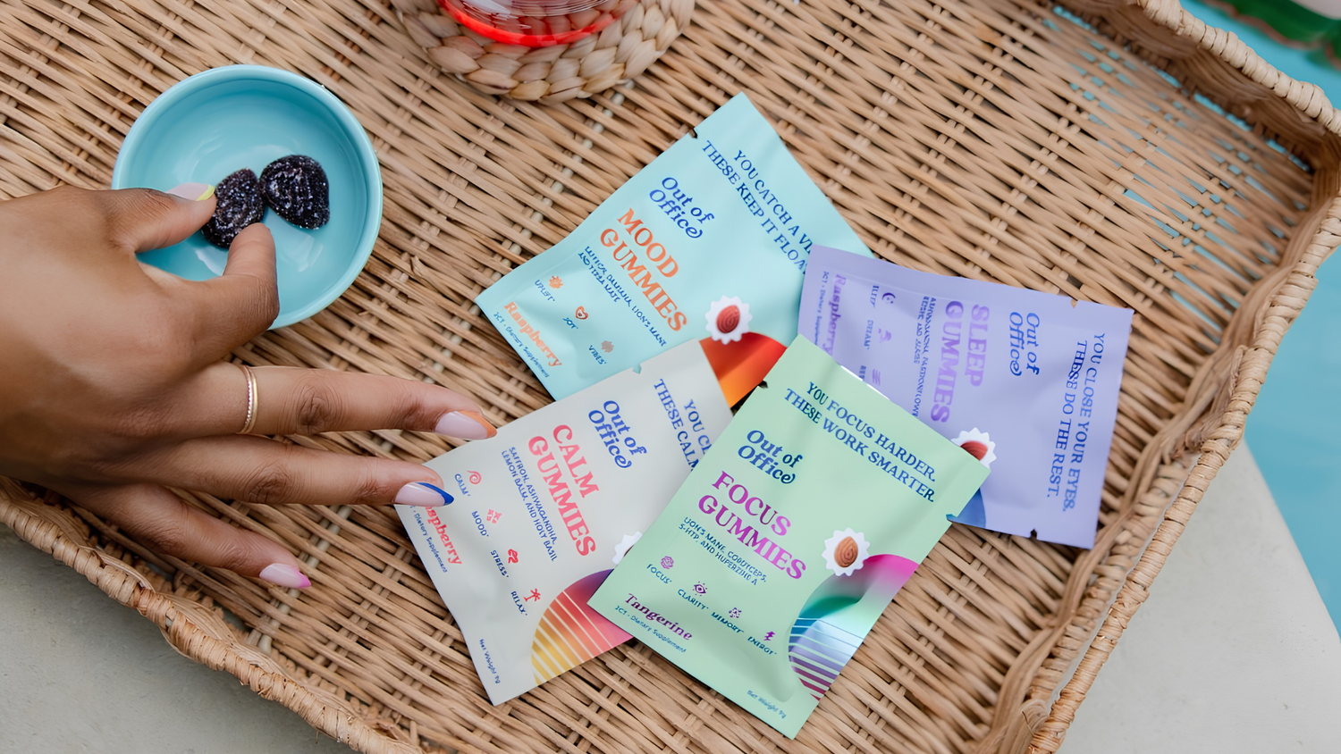 Overhead of Out of Office gummy packets in a wicker basket, with a hand picking a gummy from a small blue dish