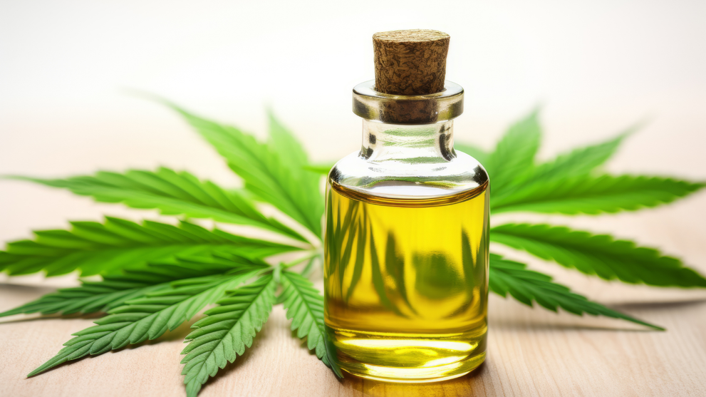 Glass bottle of golden CBD oil on a wooden surface with a cannabis leaf in the background